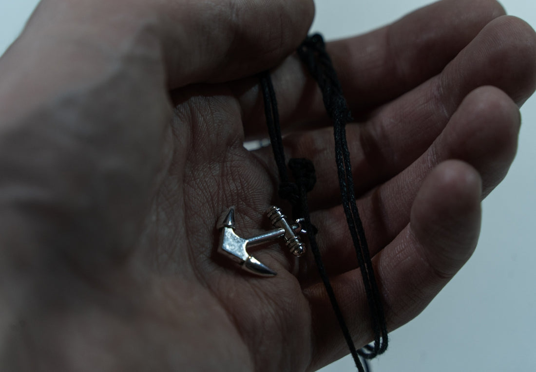Close-up of a silver anchor pendant on a black cord.