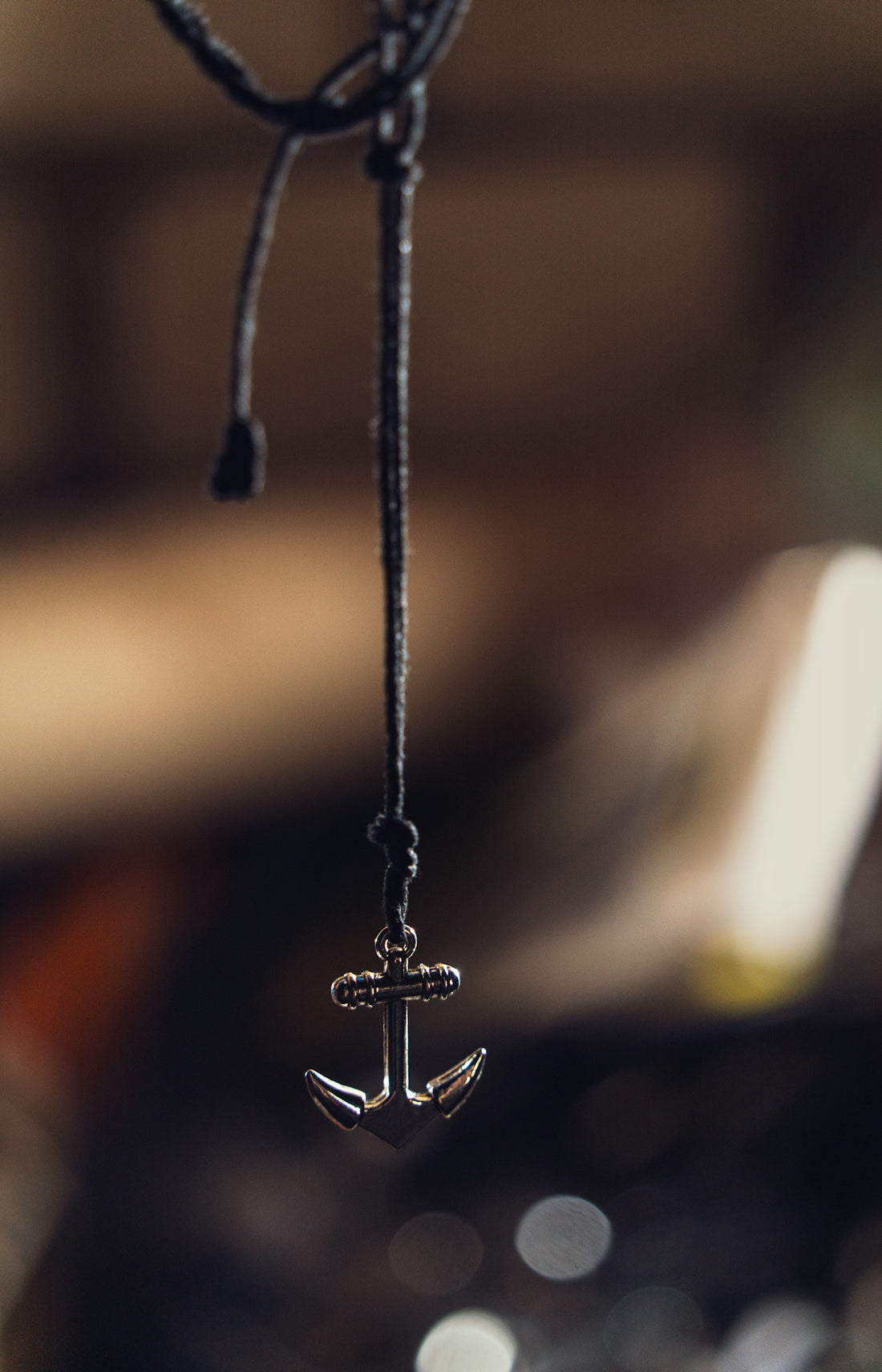 A silver anchor pendant hanging on a dark cord