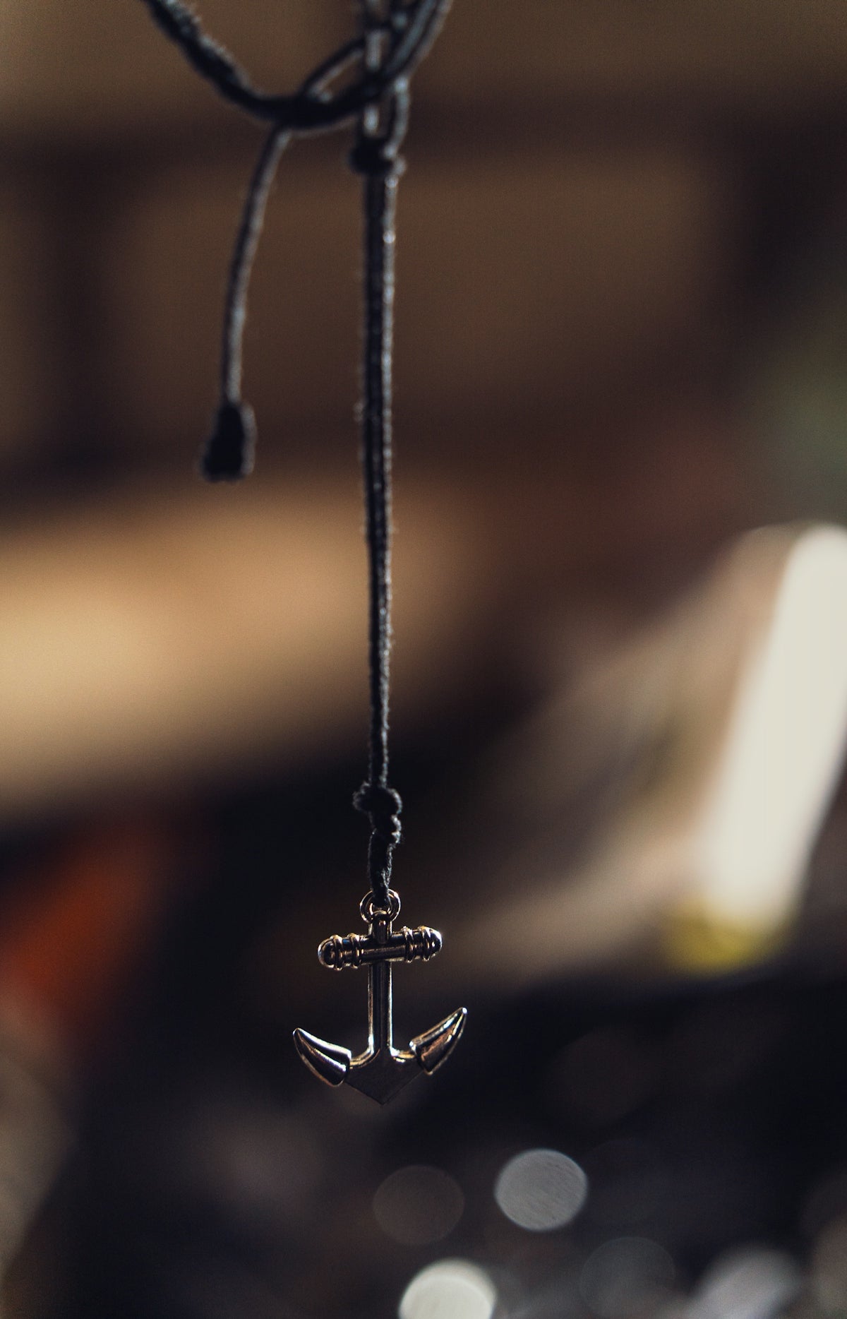 A silver anchor pendant hanging on a dark cord